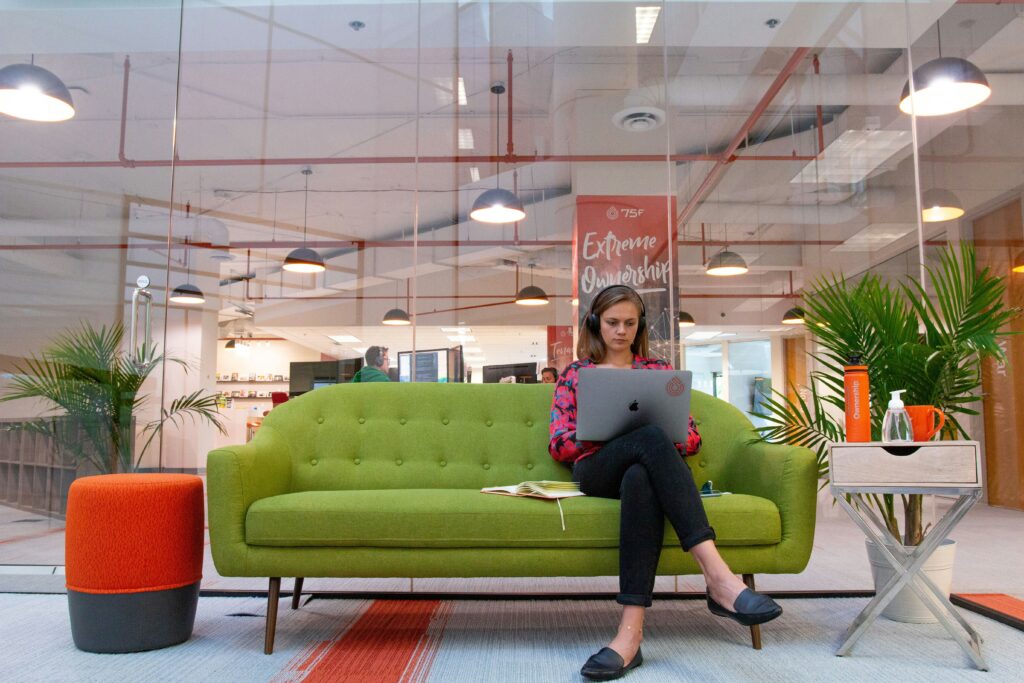 Startup founder typing on laptop on a green couch in her modern office.