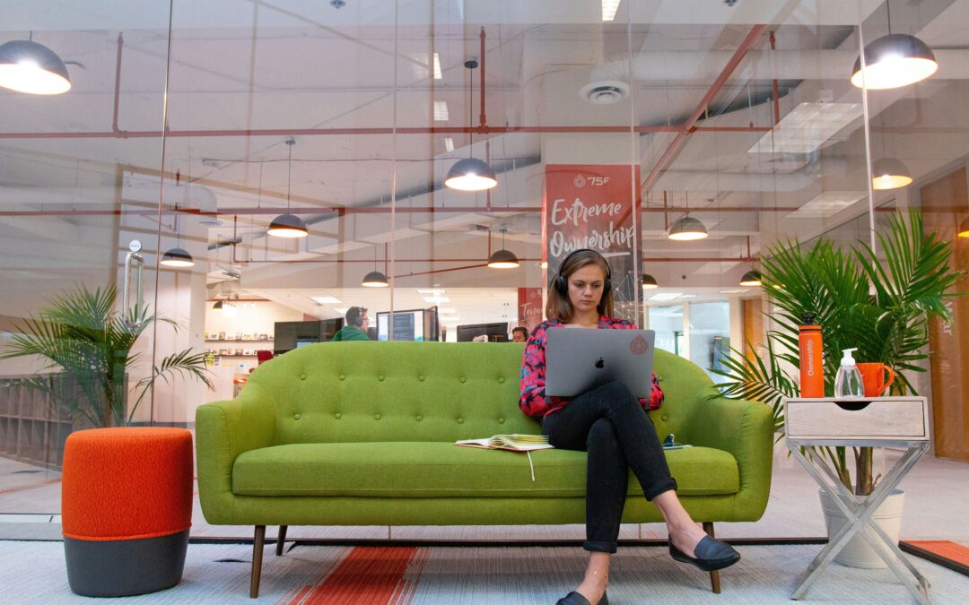 Startup founder typing on laptop on a green couch in her modern office.